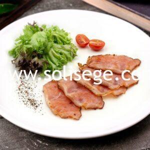 5 slices of golden brown cooked back bacon on a white round plate with lettuce and cherry tomatoes as garnish.