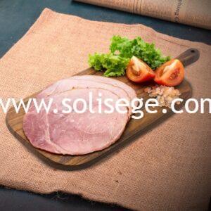 3 slices of Solisege black forest ham on a wooden board with lettuce, tomatoes, and rock salt as garnish.